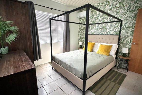 Stylish tropical bedroom at Villa Sunset in Aruba featuring a modern four-poster bed, botanical wallpaper, and luxury linens—ideal for couples on an adults-only getaway.