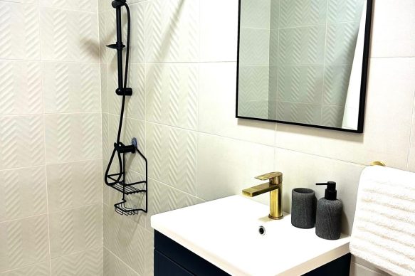 Contemporary bathroom at Villa Sunset in Aruba featuring a walk-in shower, elegant vanity with gold fixtures, and minimalist décor.