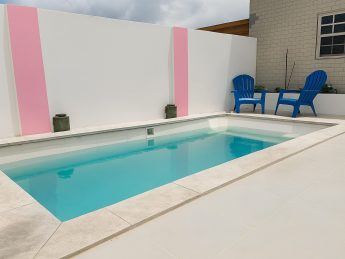 Villa Sunrise in Aruba featuring a private turquoise pool with modern white terrace and blue Adirondack chairs, designed for couples on an adults-only retreat.