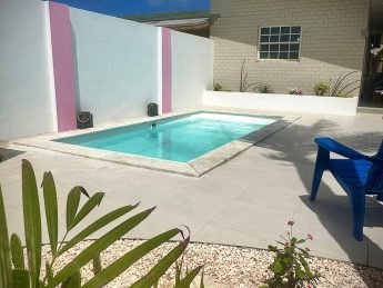 Villa Sunrise private pool in Savaneta, Aruba, with white stucco walls, pink accents, and tropical garden.