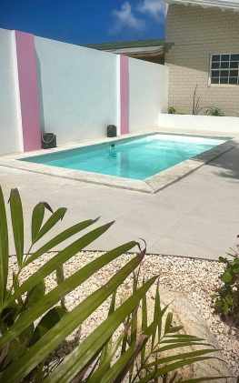 Villa Sunrise private pool in Savaneta, Aruba, with white stucco walls, pink accents, and tropical garden.