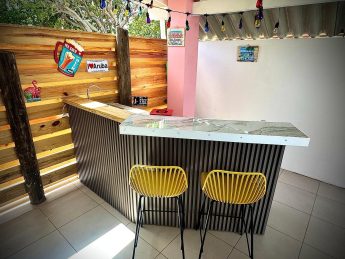 Private outdoor bar at Villa Sunrise in Aruba with marble counter, yellow chairs, and tropical decor.
