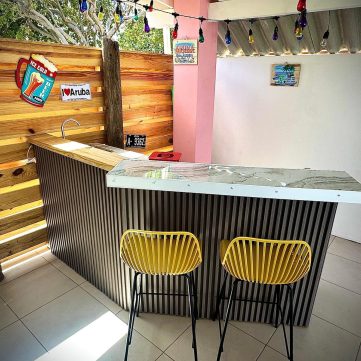 Private outdoor bar at Villa Sunrise in Aruba with marble counter, yellow chairs, and tropical decor.