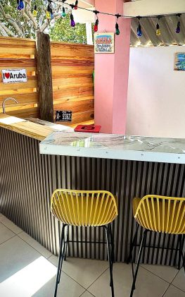 Private outdoor bar at Villa Sunrise in Aruba with marble counter, yellow chairs, and tropical decor.