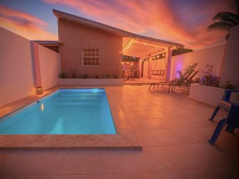 Villa Sunrise private pool at Flamingo Bay Villas in Savaneta, Aruba, lit at sunset with loungers, swings, and outdoor bar.