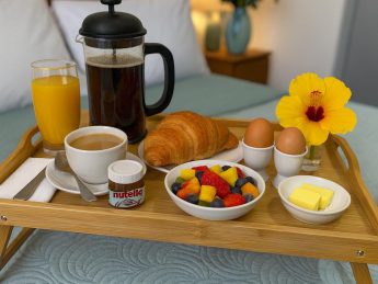 Breakfast in bed with coffee, juice, croissant, fruit, and fresh flowers at Villa Sunrise, Flamingo Bay Villas Aruba.