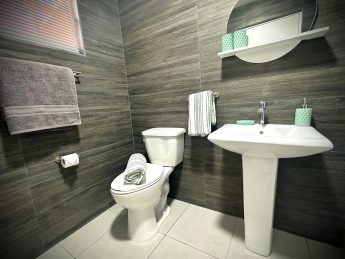 Modern bathroom at Villa Sunrise, Flamingo Bay Villas Aruba with sink, mirror, toilet, and fresh towels.