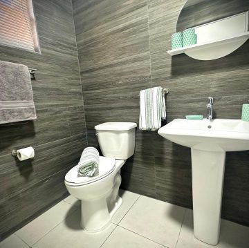 Modern bathroom at Villa Sunrise, Flamingo Bay Villas Aruba with sink, mirror, toilet, and fresh towels.