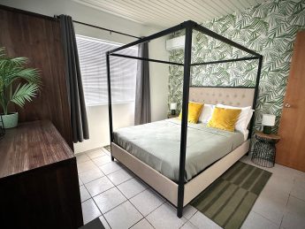 Stylish tropical bedroom at Villa Sunset in Aruba featuring a modern four-poster bed, botanical wallpaper, and luxury linens—ideal for couples on an adults-only getaway.