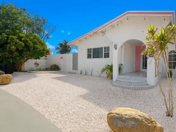 daylight, exterior front of villa, white with pink accents. tropical planting in savaneta Aruba.