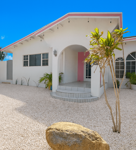 daylight, exterior front of villa, white with pink accents. tropical planting in savaneta Aruba.